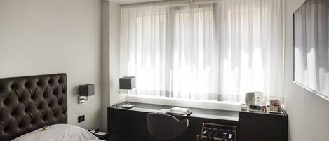 Una habitación de hotel con cama, escritorio, silla y ventana con cortinas.