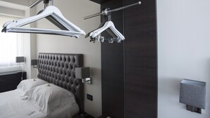 A modern hotel room with a tufted headboard, a bed with white linens, a bedside table with a lamp, and a wall-mounted light fixture. - Hotel Plaza Pescara (Pescara)