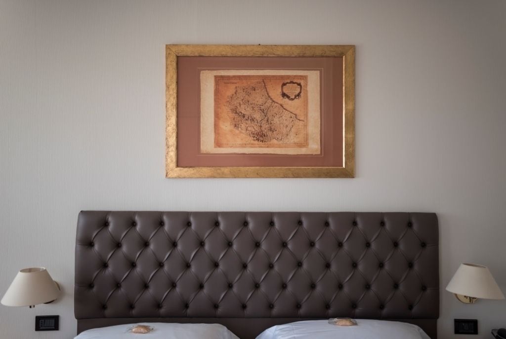 A bedroom with a tufted headboard, a framed map on the wall, and two bedside lamps.