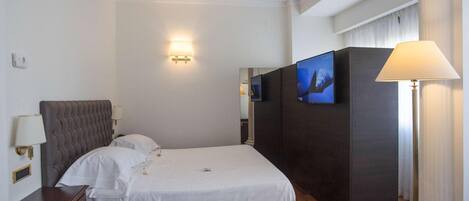 Una habitación de hotel con cama, lámparas de noche, televisión y una lámpara en una mesita.