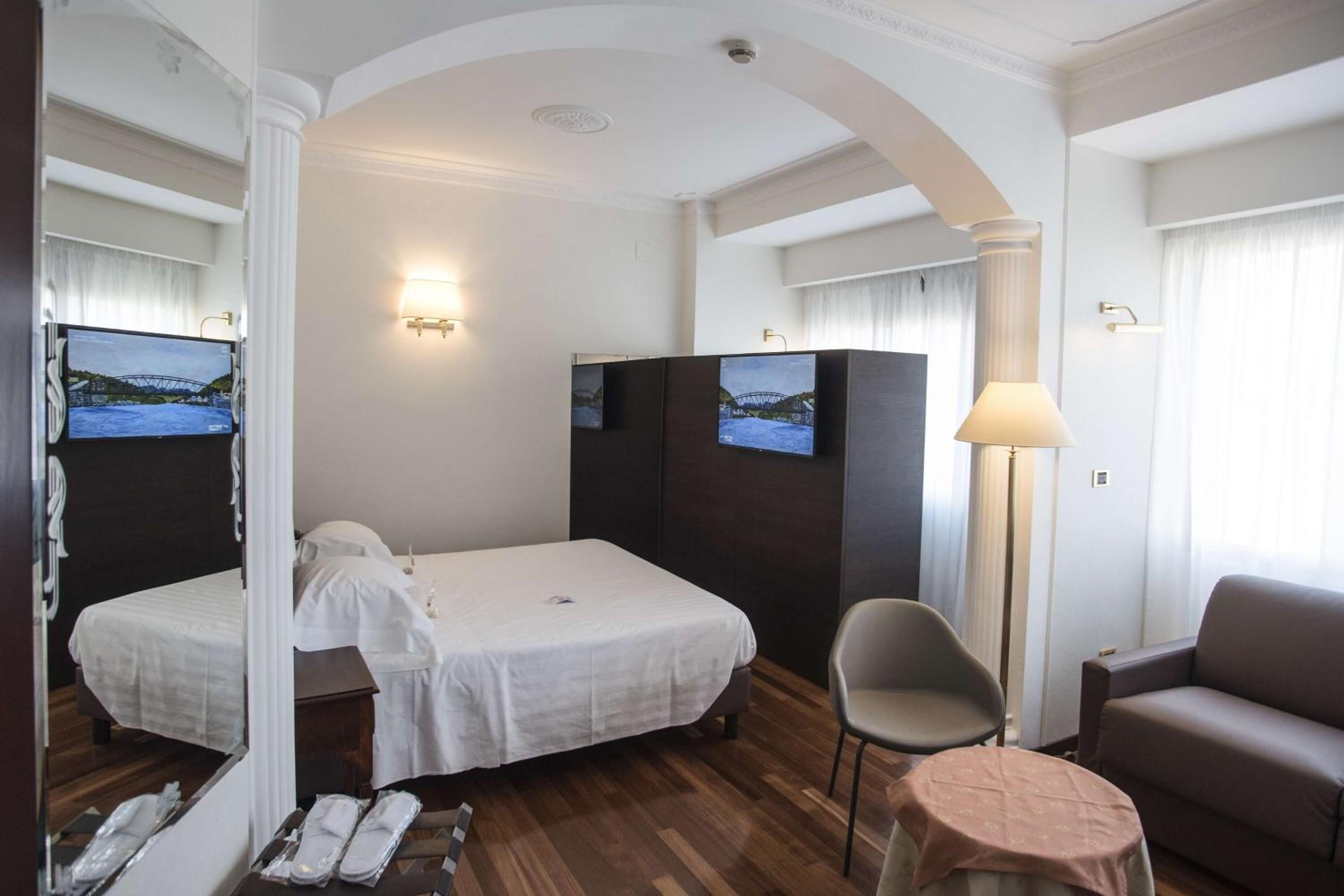 Une chambre d’hôtel avec un lit, une chaise, un canapé, une télévision et une lampe.