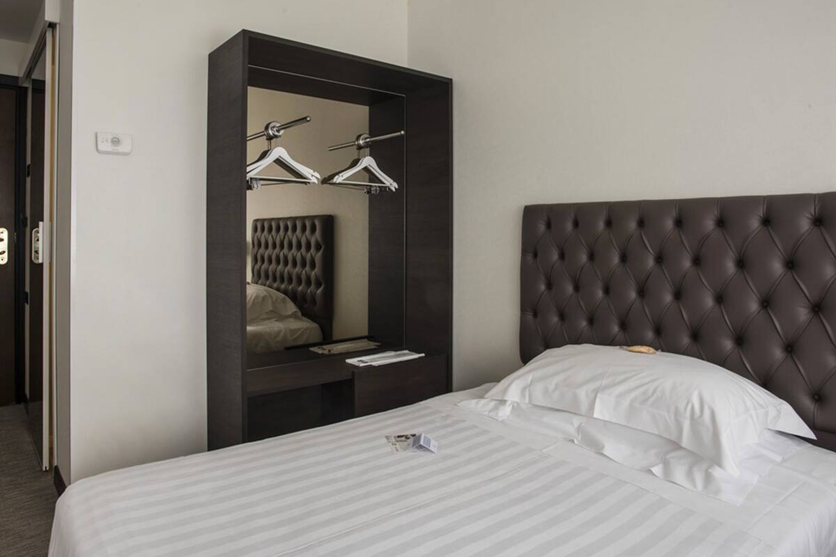 A hotel room with a large bed, a dark headboard, a wardrobe with a mirror, and a hanging clothes rack.