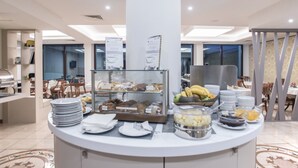 A buffet counter with various food items, including fruits, pastries, and beverages, in a well-lit dining area with tables and chairs. - Hotel Plaza Pescara (Pescara)