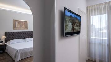 Habitació d'hotel amb un llit, una televisió penjada, un quadre amb marc a la paret i una finestra amb cortines.