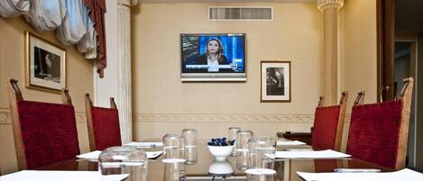 A conference room with a large table, red cushioned chairs, a television screen, and framed pictures on the walls.