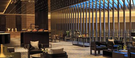 A spacious lobby with modern furniture, a reception desk, and a large window offering a view of the sky.