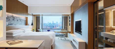 Una habitación de hotel moderna con una cama grande, un escritorio, un televisor y vistas a la ciudad.
