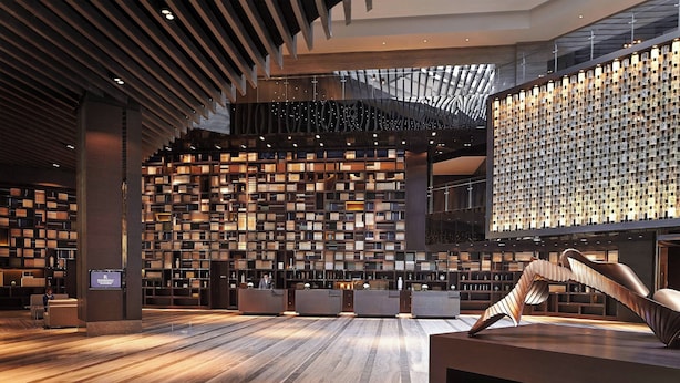 L’intérieur d’une bibliothèque moderne, avec un comptoir d’accueil central, des étagères et une sculpture métallique originale.