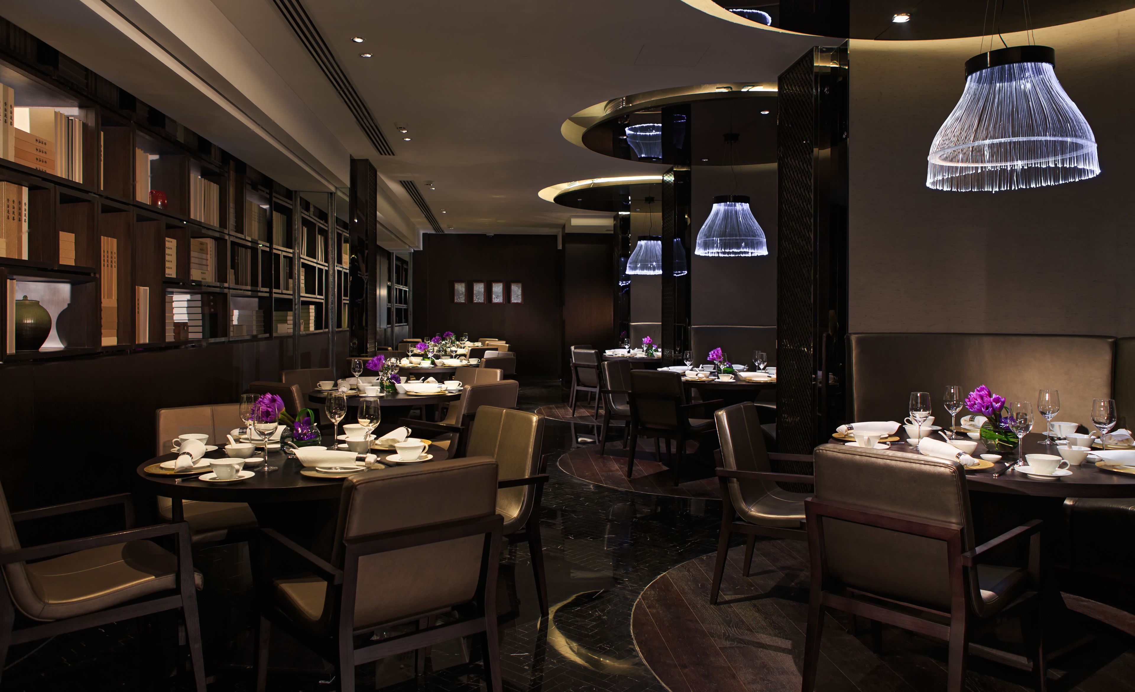 A restaurant with multiple tables, chairs, and a modern chandelier.