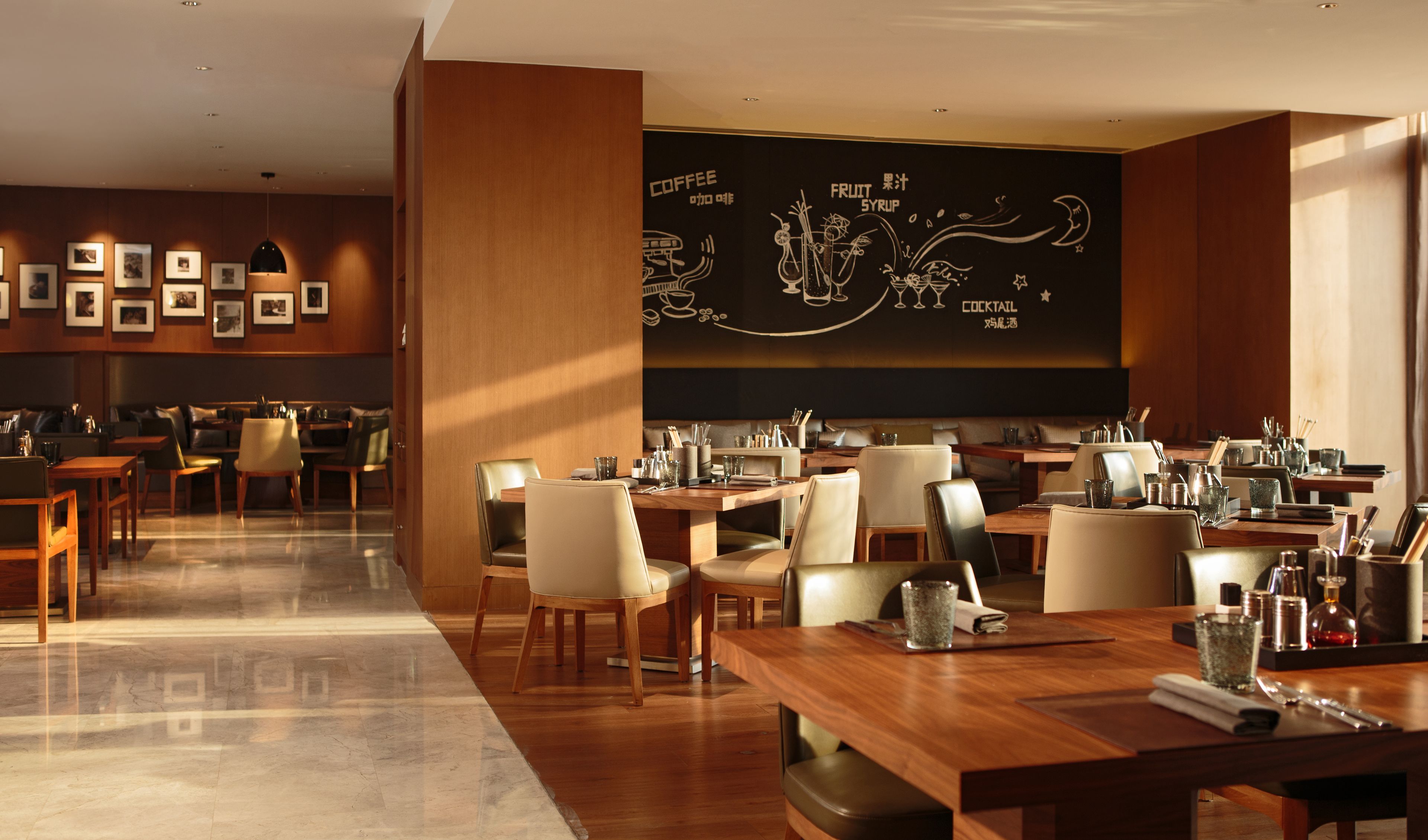A modern restaurant with wooden tables and chairs, framed pictures on the walls, and a chalkboard menu.