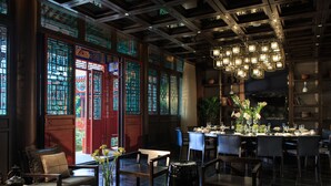 Un restaurant doté de fenêtres de style chinois traditionnel, d’un lustre moderne et d’une salle à manger où les tables sont dressées pour deux personnes.