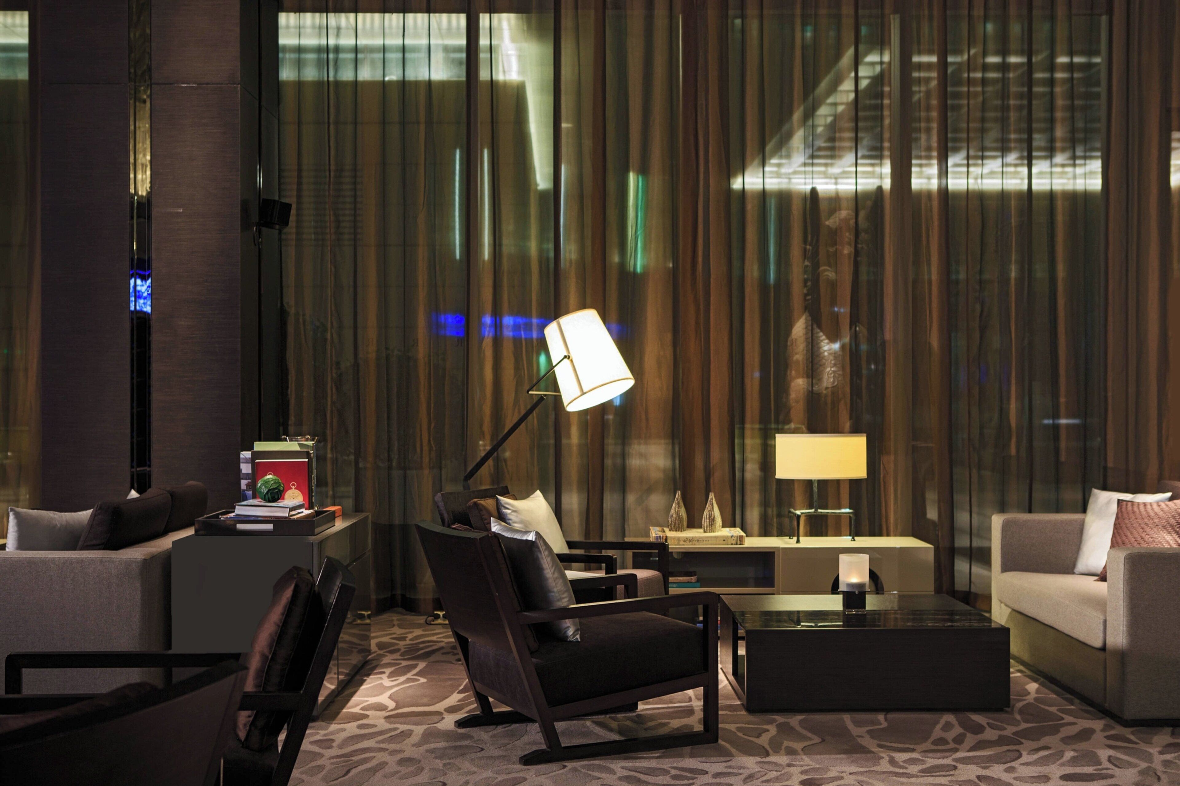Un hall d’hôtel moderne avec un canapé, des fauteuils, une table basse et une lampe.