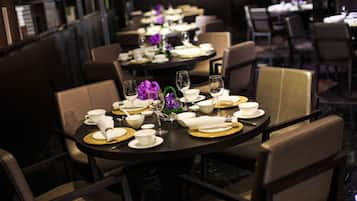 Un restaurante con mesas redondas dispuestas para comer, cada una con tazas, platillos y posavasos dorados.