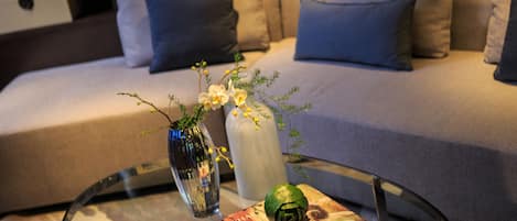 A modern living room with a glass coffee table, a sofa with cushions, and decorative items including a vase with flowers and a book.