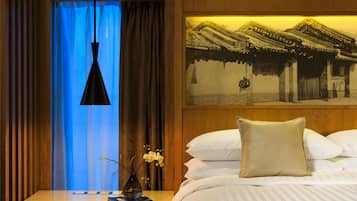 Une chambre d’hôtel avec un lit, une table de chevet, un vase de fleurs, un tableau au mur et une fenêtre illuminée d’une lumière bleue.