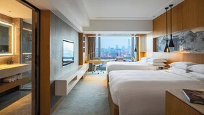 Une chambre d’hôtel moderne dotée d’un grand lit, d’un bureau et offrant une vue sur le panorama urbain.