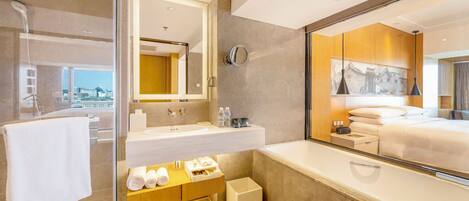 A modern hotel bathroom with a glass shower enclosure, a large mirror, a vanity with a sink, and a large bathtub.