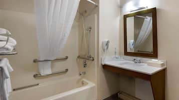 A bathroom with a bathtub, shower, handrails, a sink with a mirror, and towels.