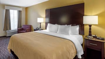 A hotel room with a large bed, a chair, a nightstand with a lamp, and a window with curtains.