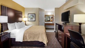 A hotel room with a bed, desk, TV, and a bathroom visible through an open door.