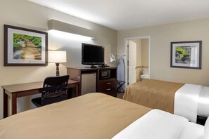 A hotel room with two beds, a desk with a chair, a television, a microwave, and a small refrigerator.