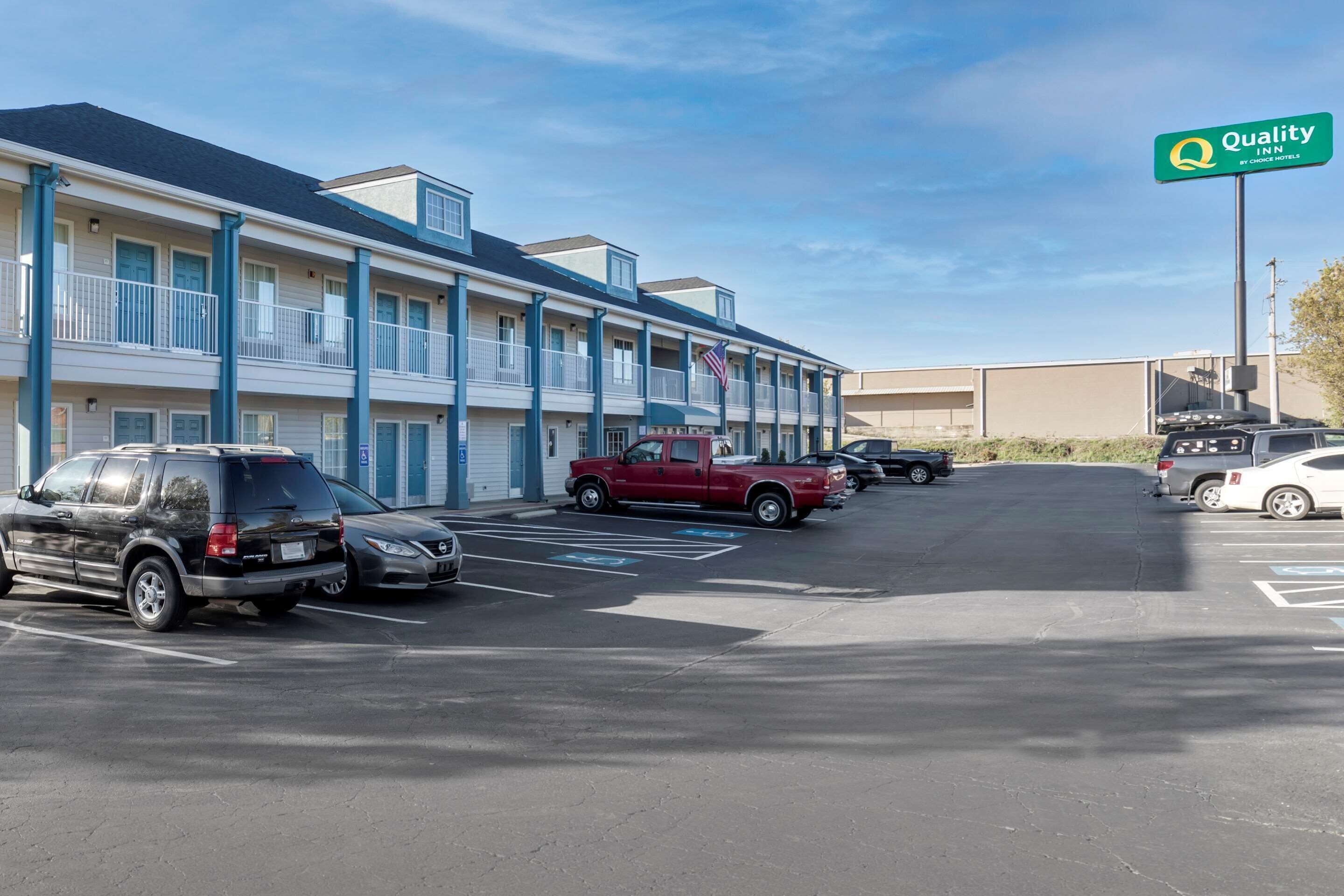 Un motel con edificios de varios pisos, un estacionamiento con varios autos y un letrero de Quality Inn by Choice Hotels.