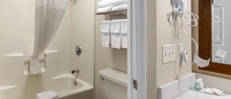A bathroom with a bathtub, toilet, and a sink with a hairdryer and towels.