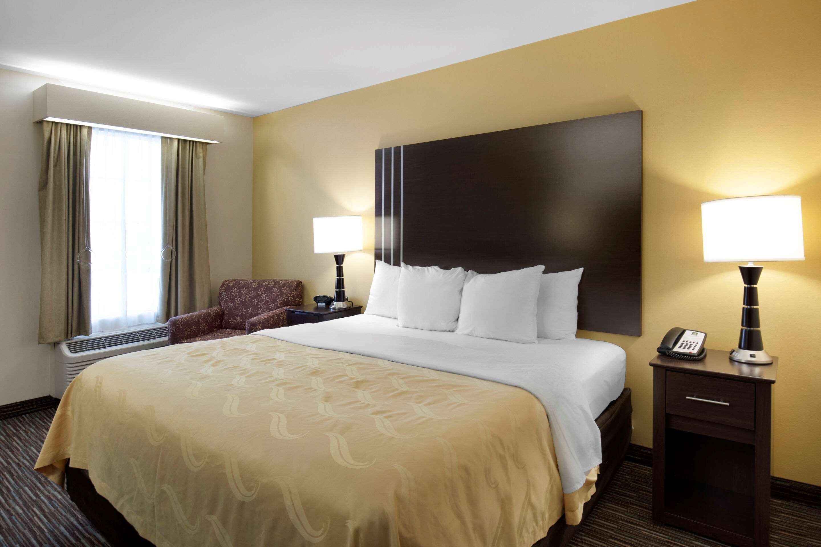 A hotel room with a large bed, two bedside lamps, a chair, and a desk with a telephone.