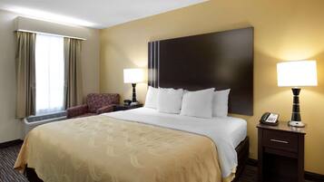 A hotel room with a large bed, two bedside lamps, a chair, and a desk with a telephone.