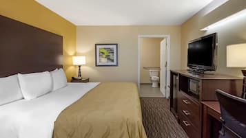 A hotel room with a bed, a television, a desk, and a bathroom visible through an open door.