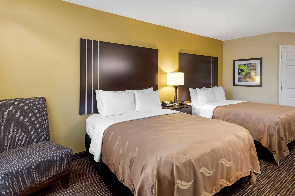 A hotel room with two beds, a chair, a lamp, and a framed picture on the wall.