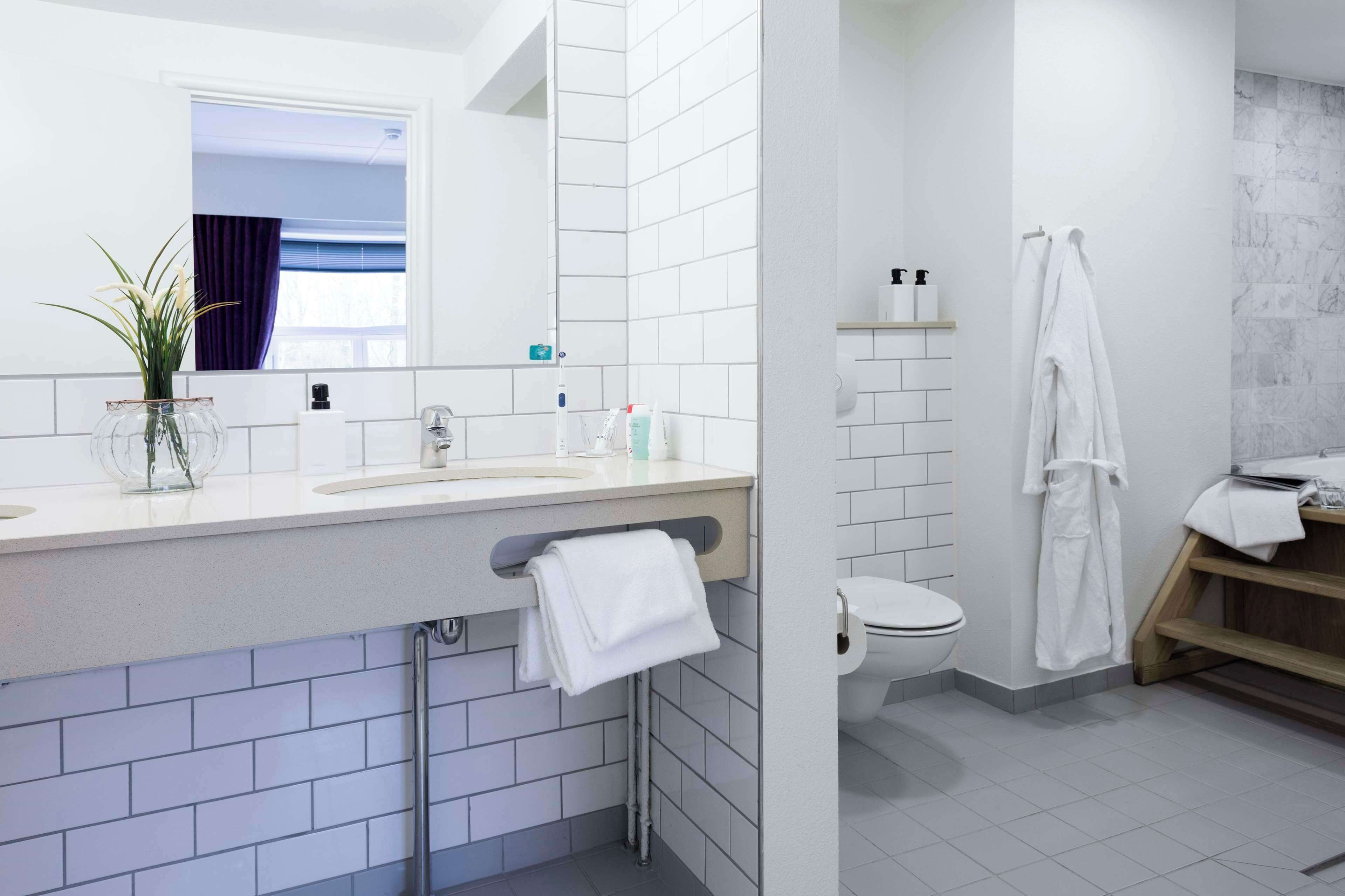 A modern bathroom with white tiles, a sink with a mirror, a toilet, and a shower area.