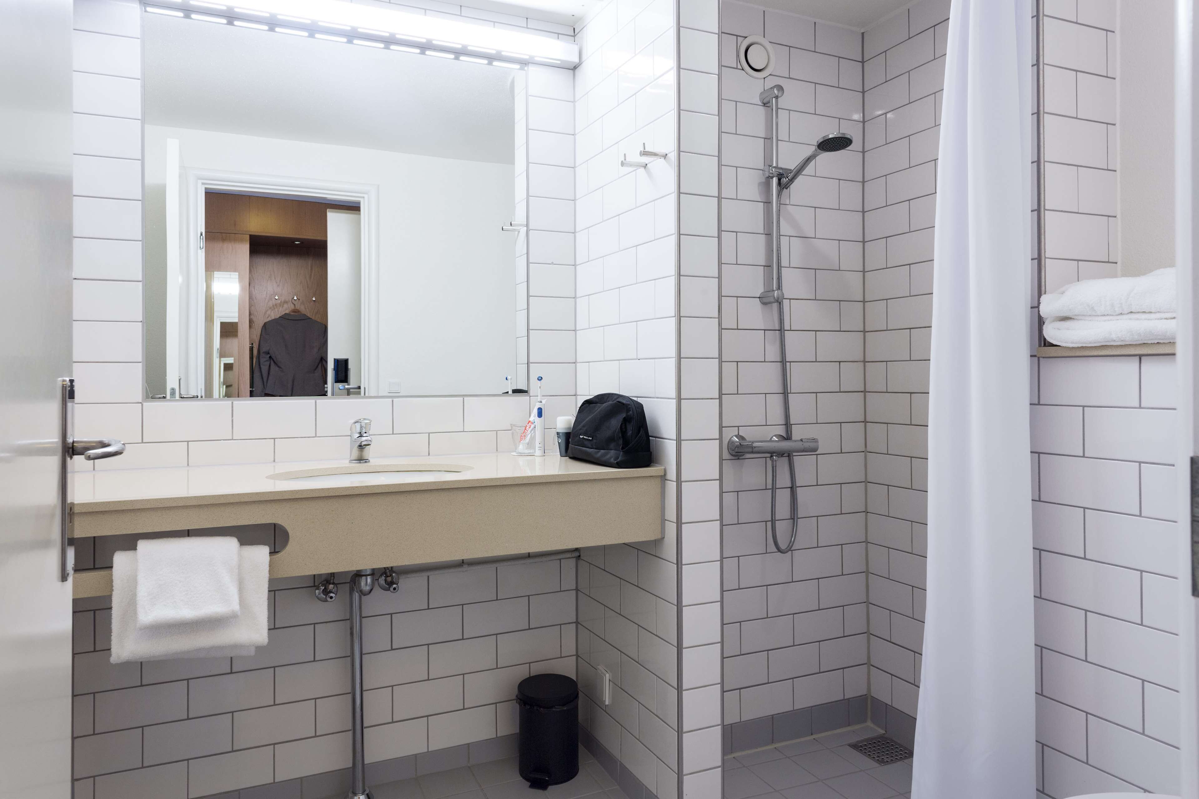 Une salle de bain moderne équipée d’un lavabo, d’un miroir, d’une douche et d’un porte-serviettes.