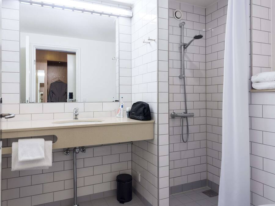 Un baño moderno con lavabo, espejo, ducha y toallero.