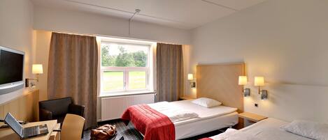 A hotel room with two beds, a desk with a laptop, a chair, a TV, and a window with curtains.