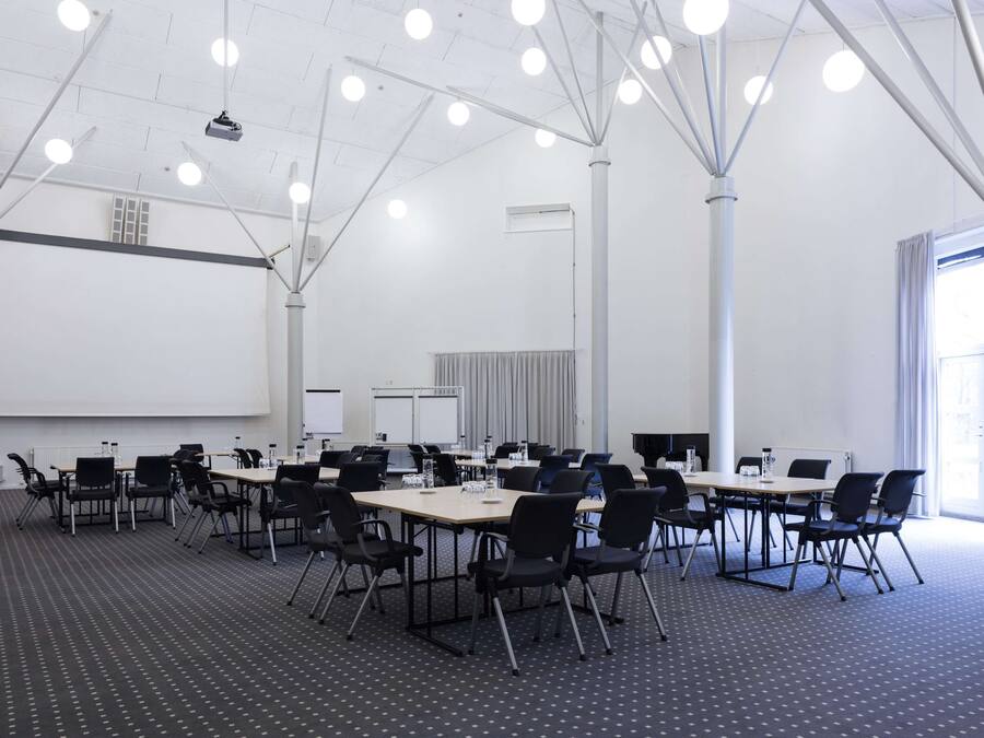 A conference room with multiple tables and chairs, a projector screen, and a large window.