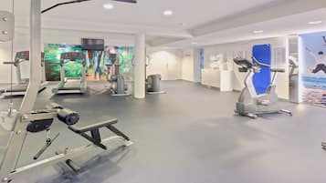 A modern gym with cardio machines, weight training equipment, and a large screen displaying exercise videos.