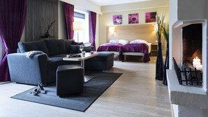 A modern hotel room with a sofa, a dining table, a fireplace, and a bed with a headboard. - Scandic Sønderborg (Sønderborg)