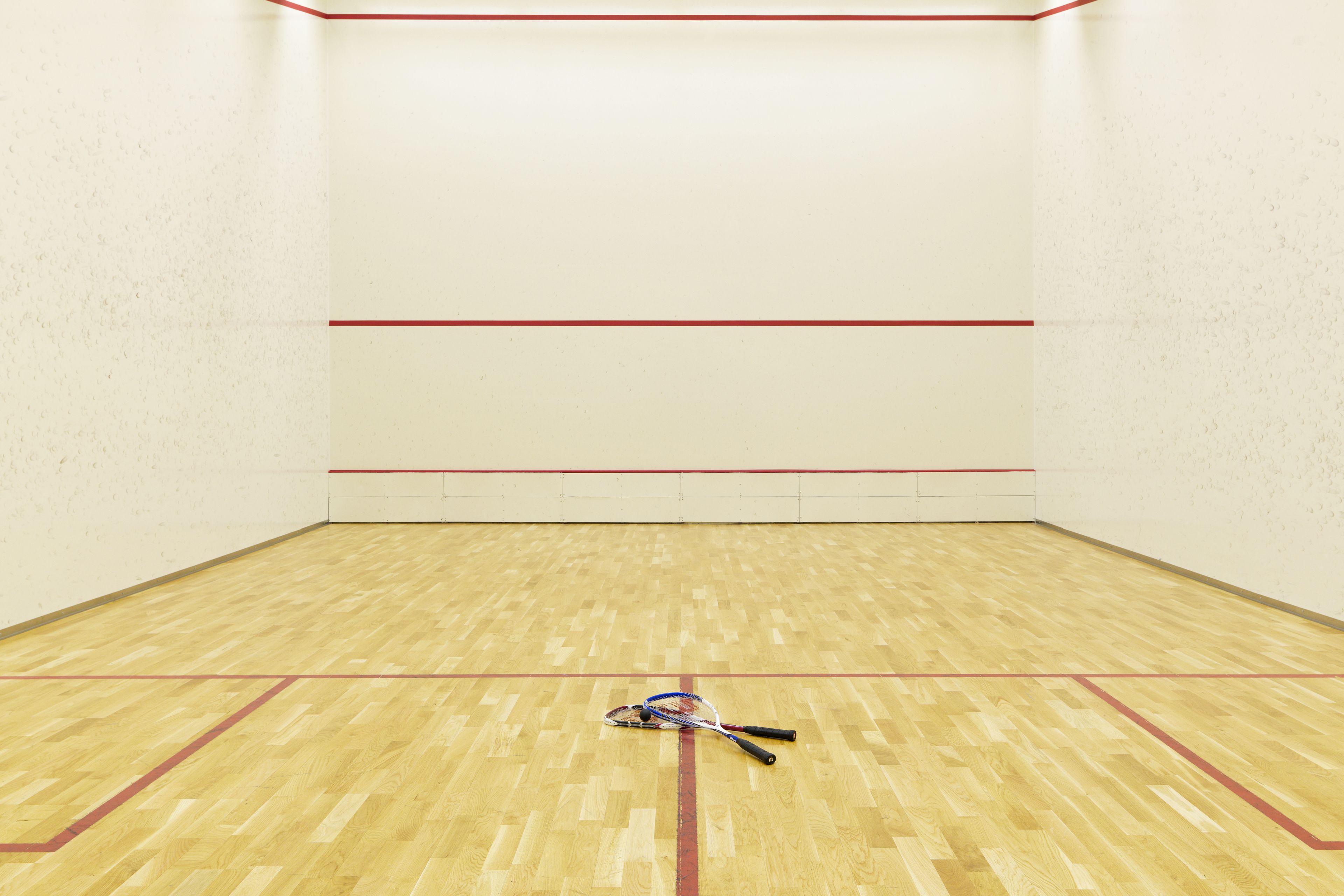 Una cancha de squash con suelo de madera y líneas delimitadoras rojas.
