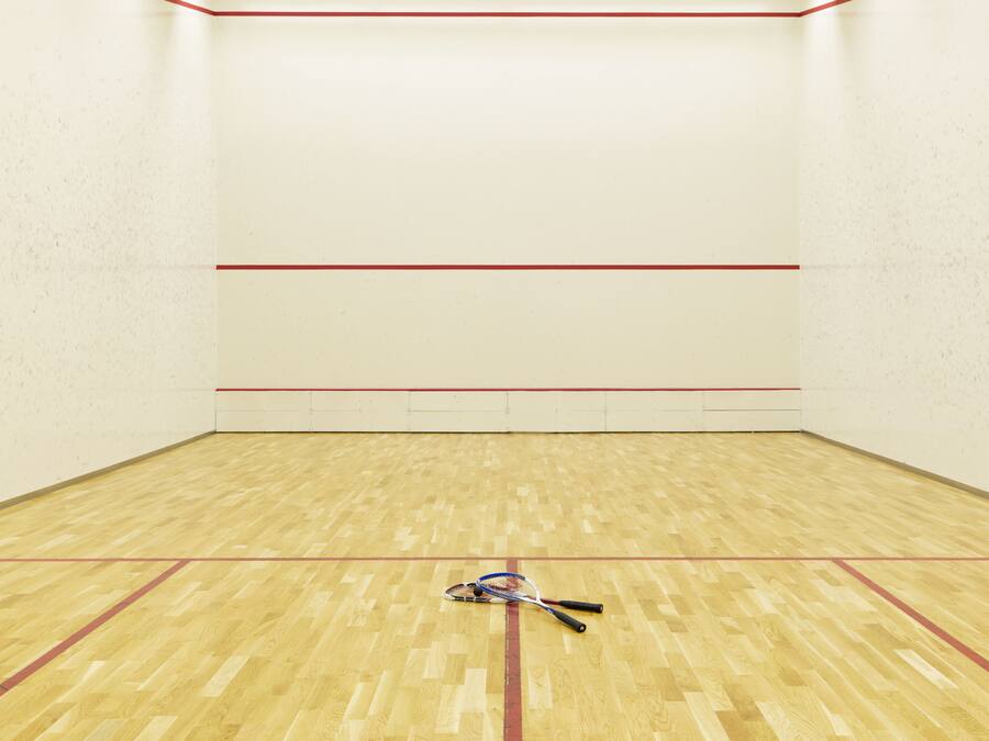 Una cancha de squash con suelo de madera y líneas delimitadoras rojas.