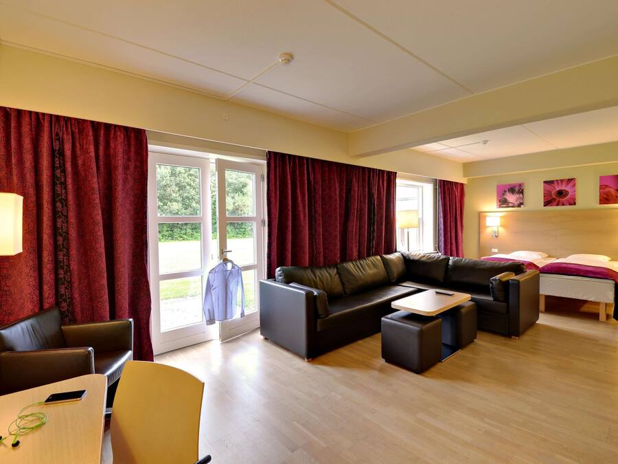 Una habitación de hotel moderna con sofá, una mesa de comedor, una pequeña cocina y una cama.