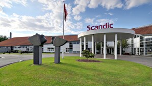 A Scandic hotel with a modern design, featuring a circular structure with columns, a flag, and a well-maintained lawn. - Scandic Sønderborg (Sønderborg)