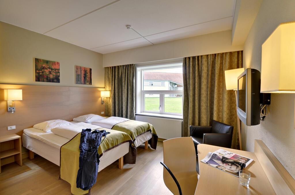 A hotel room with two beds, a desk, a chair, and a TV.