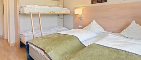 A hotel room with a bunk bed, a single bed, and a nightstand with a lamp.