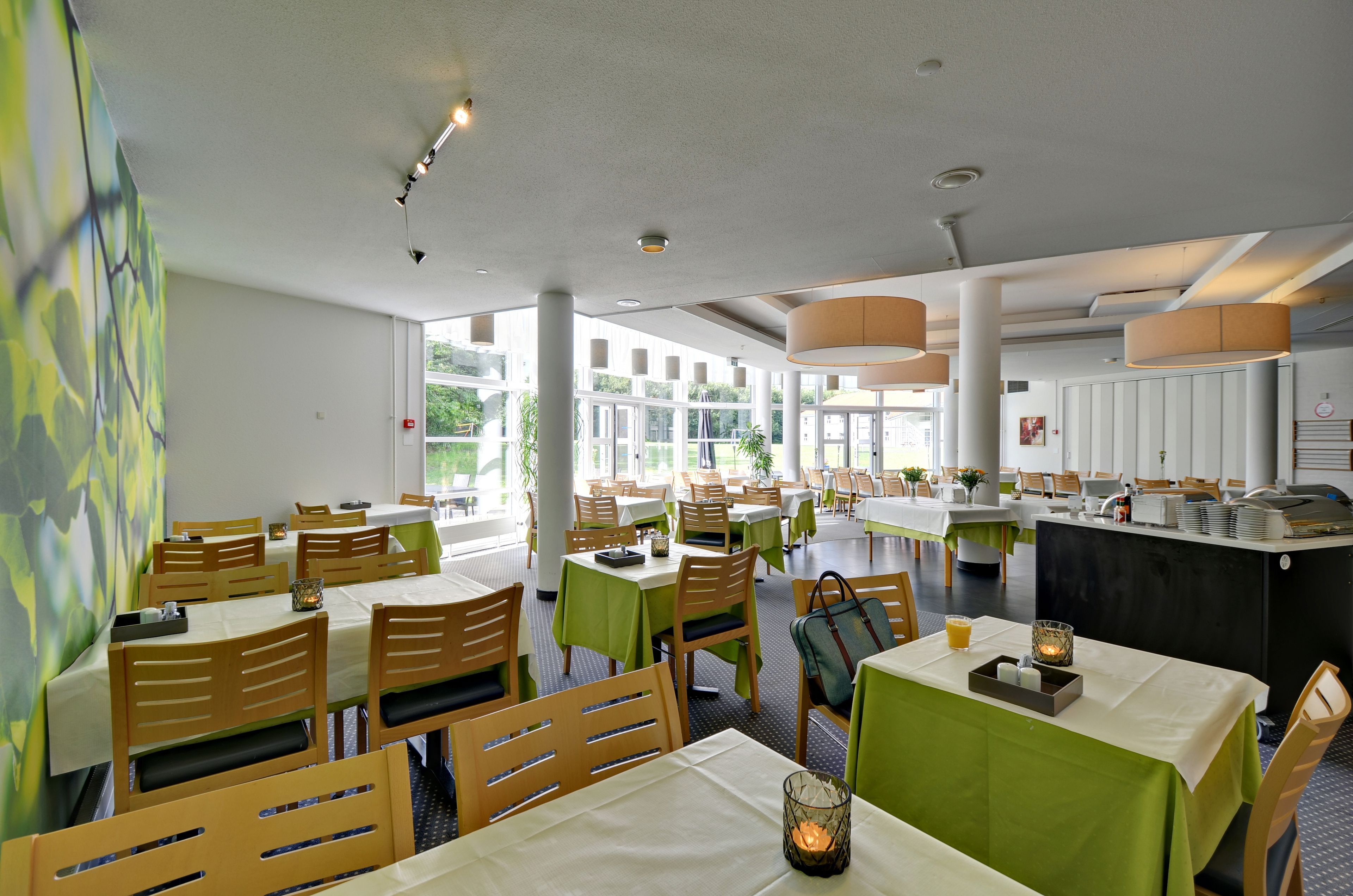 En rummelig restaurant med flere borde og stole, store vinduer og et centralt barområde.