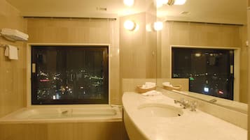 A modern bathroom with a bathtub, a sink, and a large mirror reflecting a cityscape view.