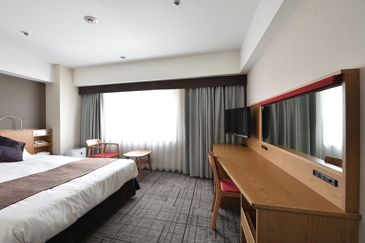 A hotel room with a bed, a desk, a chair, a television, and a window with curtains.