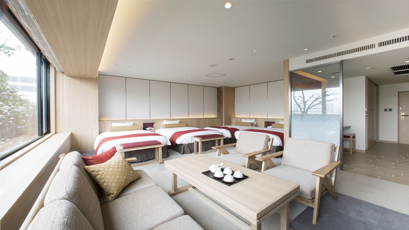 Une chambre d’hôtel moderne avec un canapé, deux lits, une table à manger et une vue sur la ville.