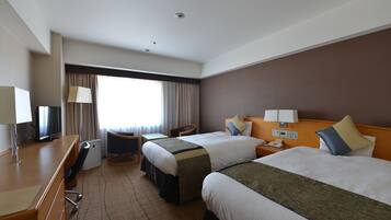 Habitación de hotel con dos camas, un escritorio, una silla, un televisor y una ventana con cortinas.