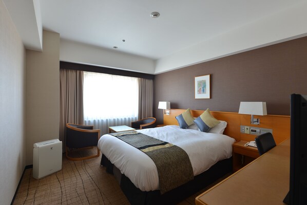 Habitación de hotel con una cama grande, un escritorio, una silla, una mesita, una lámpara, un cuadro en la pared y una ventana con cortinas.